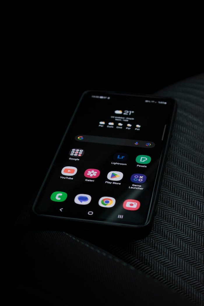 Close-up of a smartphone displaying apps and weather on a dark background.