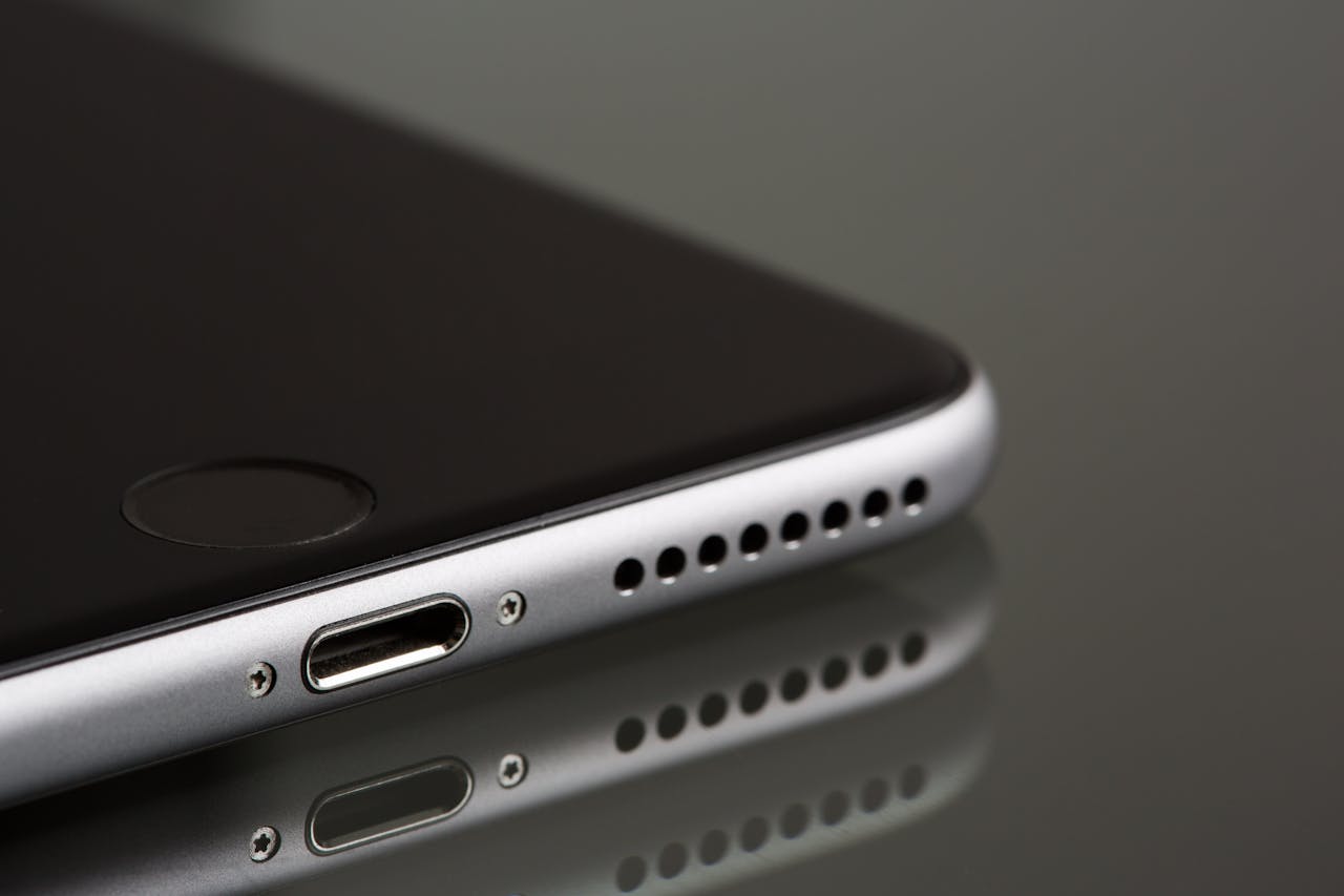 A sleek smartphone close-up highlighting its lightning connector and speaker, reflecting on a surface.