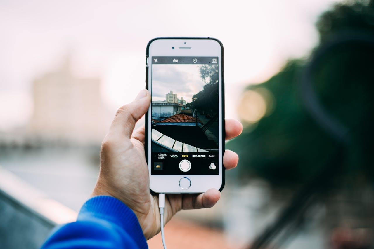 Close-up of a hand holding a smartphone while capturing a cityscape outdoors.